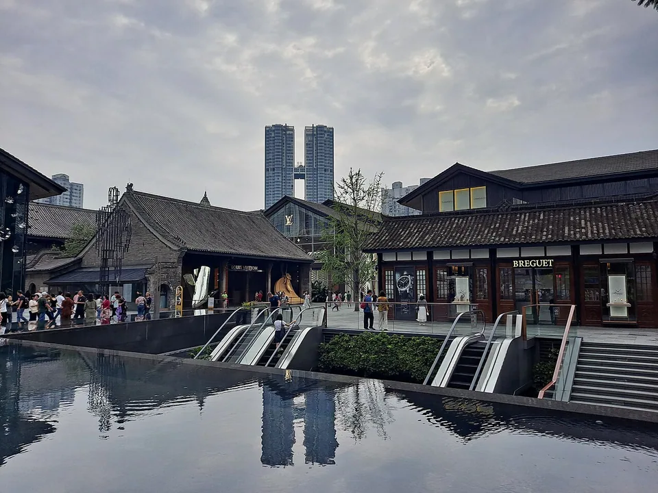 成都太古里的坡屋顶商业建筑、步行空间、扶梯、楼梯与前景水面。